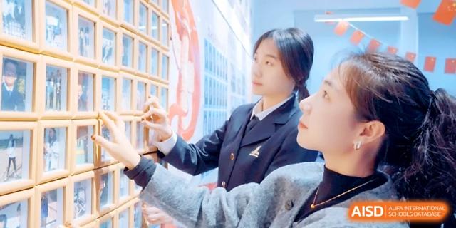 Two students in formal uniforms work together on a creative wall display in a school hallway at Maple Leaf International School - Xi_an.