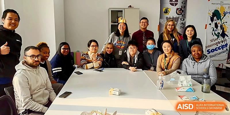 A large group of students and international faculty pose for a photo around a white conference table at Maple Leaf International School - Xi_an.