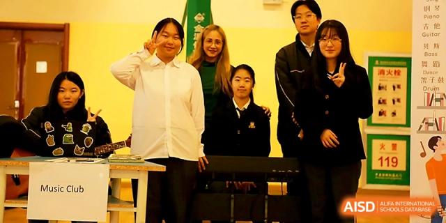 A group of students and a teacher pose for a photo near a piano in a music or performance room at Maple Leaf International School - Xi_an.
