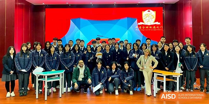 A large class of students in blue uniforms and their teachers pose in front of a blue backdrop at Maple Leaf International School - Xi_an.