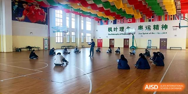 A teacher leads a physical education or health session for students on a large indoor gym floor at Maple Leaf International School - Xi_an.