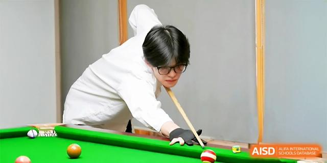 A student focused on aiming a shot during a billiards or pool game at Maple Leaf International School - Xi_an.