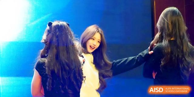 A female student with long hair smiling during a stage performance at Maple Leaf International School - Xi_an.