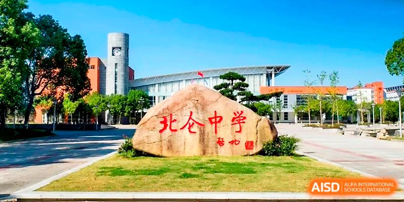 A large ceremonial rock with red inscriptions stands in front of the modern campus entrance at Ningbo Beilun High School.