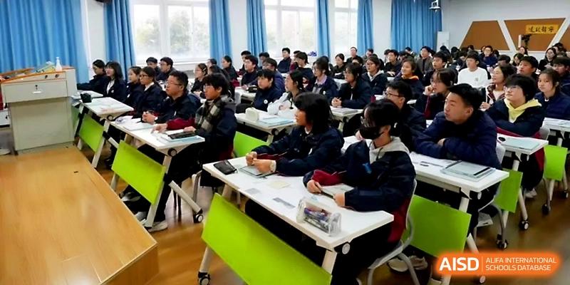 Students sit in neat rows during a lecture, focusing on their notebooks and the teacher in front at Ningbo Beilun High School.