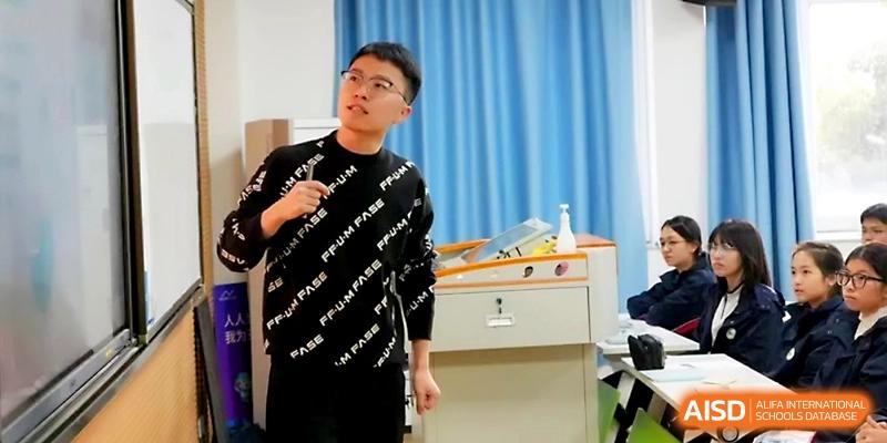 A male teacher in a black sweater leads an energetic classroom discussion with his students at Ningbo Beilun High School.