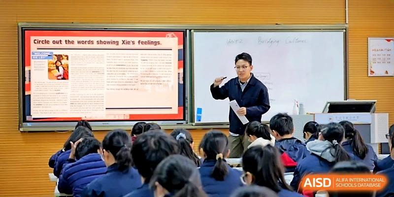 A male educator gestures toward a digital screen during an interactive English language lesson at Ningbo Beilun High School.