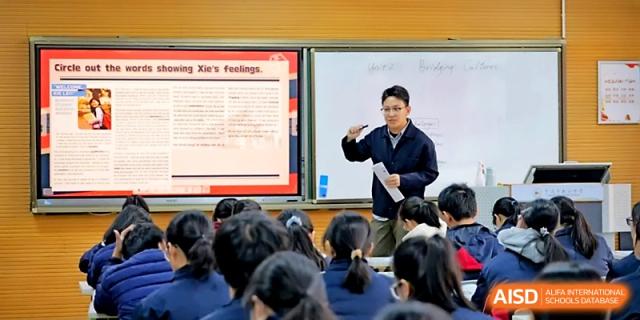 A male educator gestures toward a digital screen during an interactive English language lesson at Ningbo Beilun High School.
