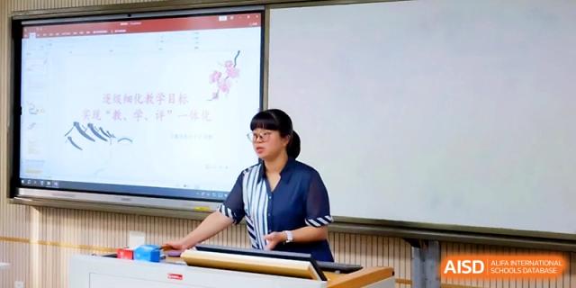 A female teacher in a striped shirt facilitates a classroom activity using a digital display at Ningbo Beilun High School.