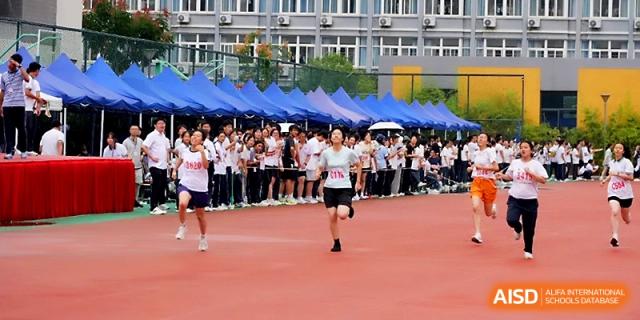 Two runners compete side-by-side during a middle-distance track event on sports day at Ningbo Beilun High School.