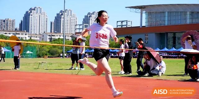 A female student runs a long-distance race with determination on a clear, sunny day at Ningbo Beilun High School.