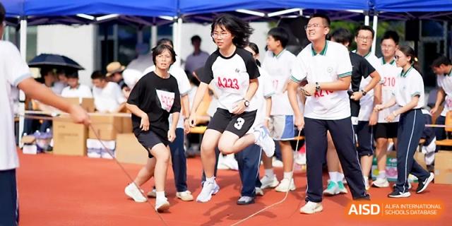 A student jumps for a high jump attempt while a teacher observes the form and height at Ningbo Beilun High School.