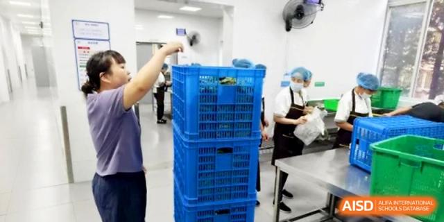 Workers in hairnets and masks organize food supply crates in the school's storage area at Ningbo Beilun High School.