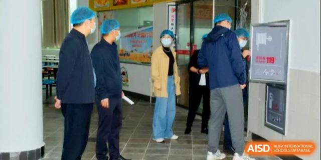 Health inspectors and staff discuss kitchen sanitation protocols in the school canteen at Ningbo Beilun High School.