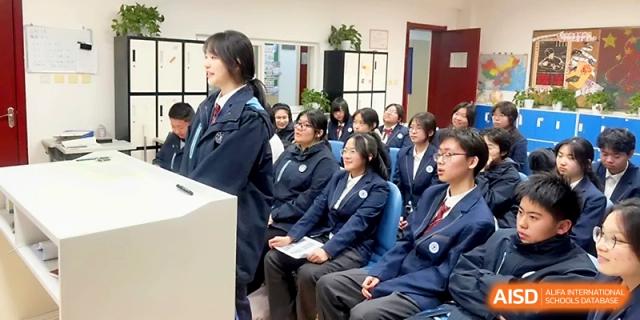 A female student in a navy uniform stands to answer a question during a classroom discussion with her peers at The High School Affiliated to Xi_an Jiaotong University.