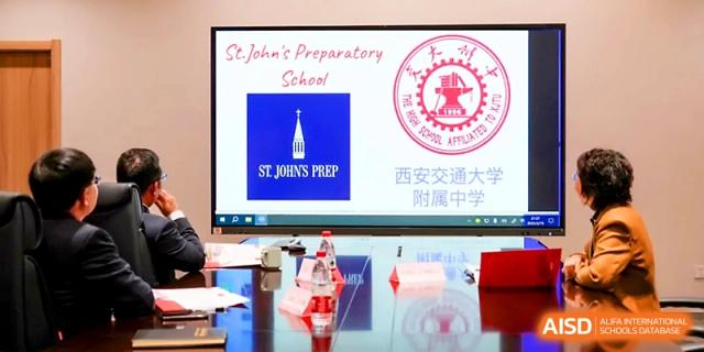 A digital display shows logos for St. John's Preparatory School and the Chinese host institution during an event at The High School Affiliated to Xi_an Jiaotong University.