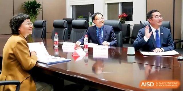 A smiling school official in a suit sits at a large conference table for a formal meeting or academic exchange at The High School Affiliated to Xi_an Jiaotong University.
