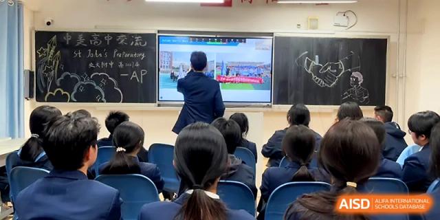 A teacher stands at the front of a classroom pointing to a digital screen during a multimedia-enhanced lesson at The High School Affiliated to Xi_an Jiaotong University.