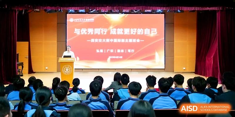 A wide shot of a lecture hall where students face a large screen displaying an orange and white presentation at The High School Affiliated to Xi_an Jiaotong University.