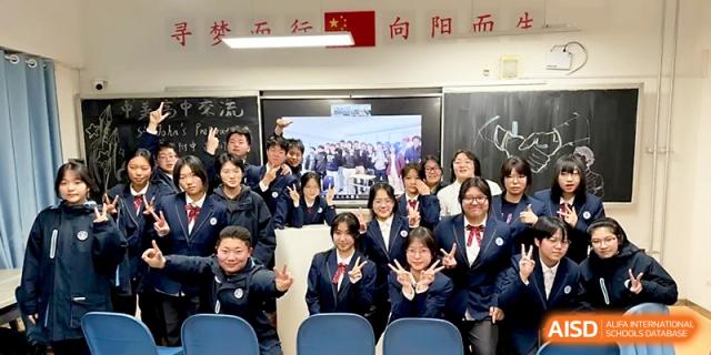 A large group of students in navy uniforms poses for a joyful group photo inside a classroom at The High School Affiliated to Xi_an Jiaotong University.