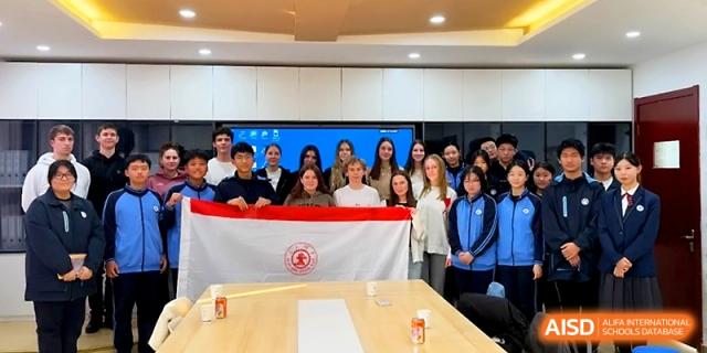 International and local students stand together holding a school flag in a modern meeting room at The High School Affiliated to Xi_an Jiaotong University.