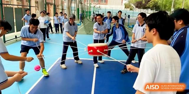 Students participate in a team-building exercise using ropes to balance a large red drum on an outdoor blue court at The High School Affiliated to Xi_an Jiaotong University.
