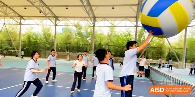 Students engage in a competitive volleyball game under an outdoor canopy during a physical education session at The High School Affiliated to Xi_an Jiaotong University.