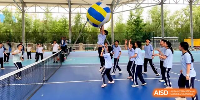 A student jumps high to hit a volleyball over the net during an outdoor match on the school's blue athletic courts at The High School Affiliated to Xi_an Jiaotong University.