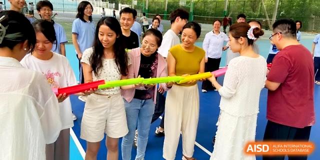 A group of female students and staff laugh while participating in a relay game with colorful tubes outdoors at The High School Affiliated to Xi_an Jiaotong University.