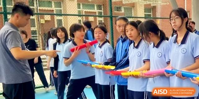 Students in blue uniforms work together to pass a ball through a series of colorful plastic tubes in a race at The High School Affiliated to Xi_an Jiaotong University.