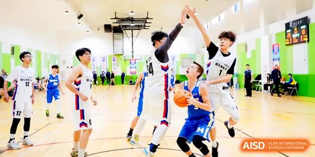 Players compete intensely under the basket during a boys' basketball game in the well-lit school sports hall at The High School Affiliated to Xi_an Jiaotong University.