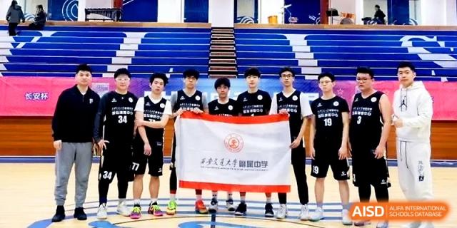 A basketball team in black uniforms stands together on the court holding a large white and red school flag at The High School Affiliated to Xi_an Jiaotong University.