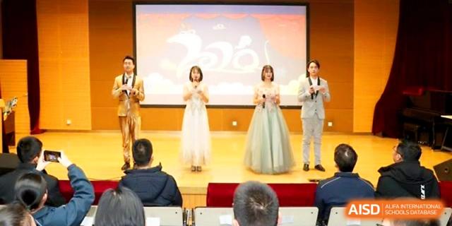 Four presenters in formal evening wear stand on stage in front of a large screen during a school gala or ceremony at The High School Affiliated to Xi_an Jiaotong University.