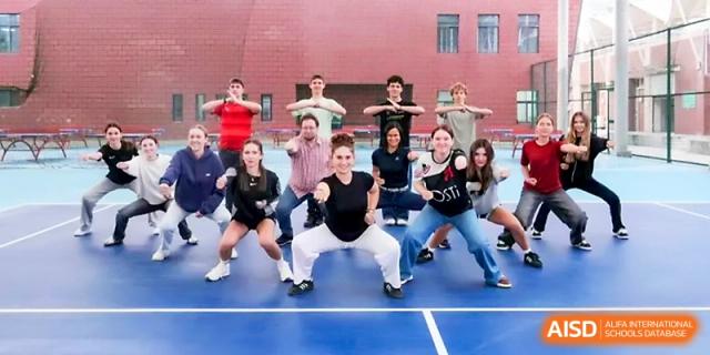 A diverse group of students in casual attire practices a synchronized dance routine on an outdoor blue court at The High School Affiliated to Xi_an Jiaotong University.