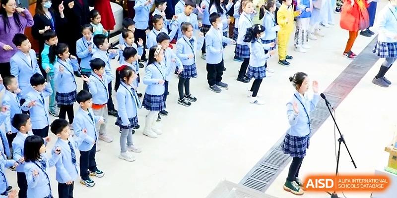 A large group of primary students in blue uniforms stand in rows during a school assembly or performance at Wahaha International School.