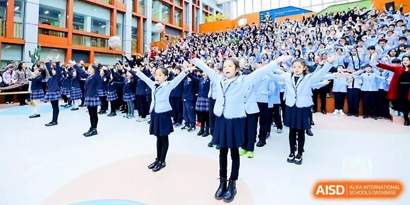 Students in uniforms perform a choreographed routine with their arms raised during a large event at Wahaha International School.