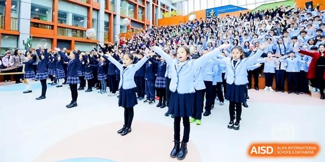 Students in uniforms perform a choreographed routine with their arms raised during a large event at Wahaha International School.