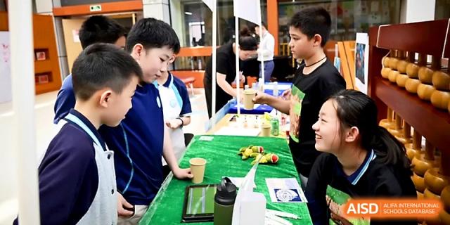Students interact with a hands-on science display featuring greenery and tablets on a green table at Wahaha International School.