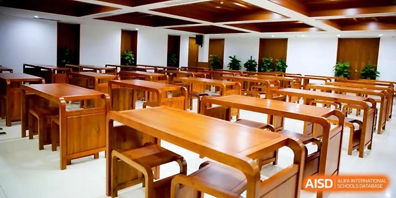 A clean and modern school cafeteria features long wooden tables and matching stools at Wahaha International School.