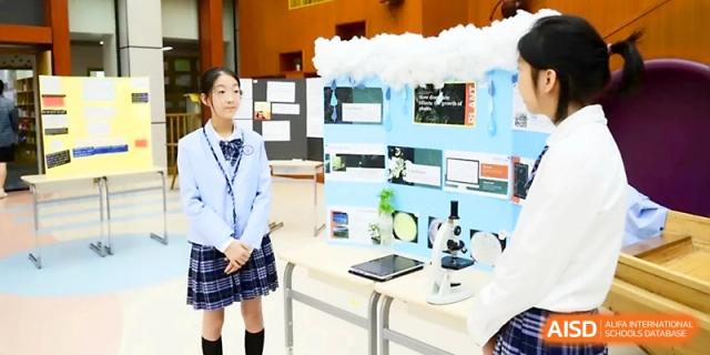 A student stands ready to present her science project involving a microscope and display at Wahaha International School.
