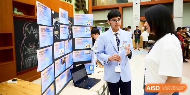 A student in a formal blazer presents his project next to a detailed display board at Wahaha International School.