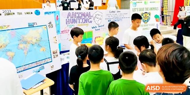 A group of students gathers around an educational poster titled "Animal Hunting" at Wahaha International School.