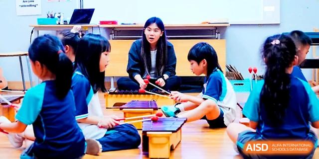 A teacher instructs two students on how to play wooden xylophones in a music room at Wahaha International School.