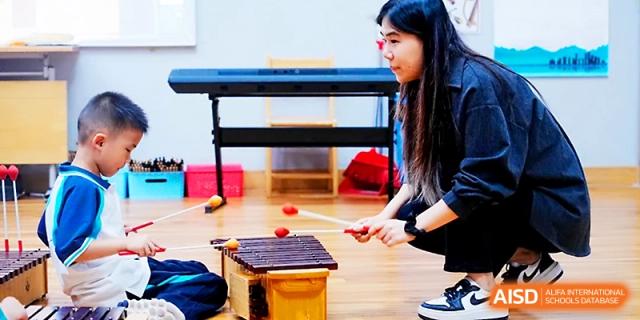 A student practices playing a percussion instrument under the guidance of a teacher at Wahaha International School.
