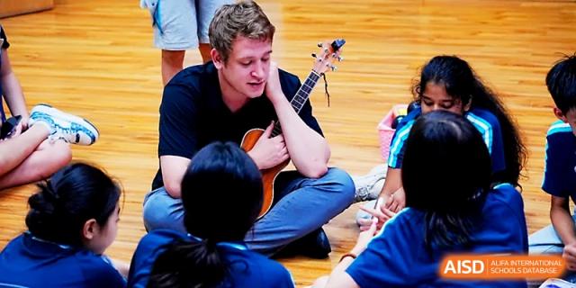 A teacher plays a ukulele while sitting on the floor with students during a music lesson at Wahaha International School.