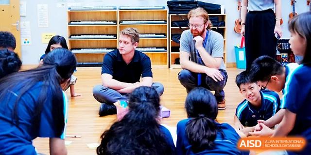 Two teachers sit on the floor and engage with a group of students during a classroom session at Wahaha International School.