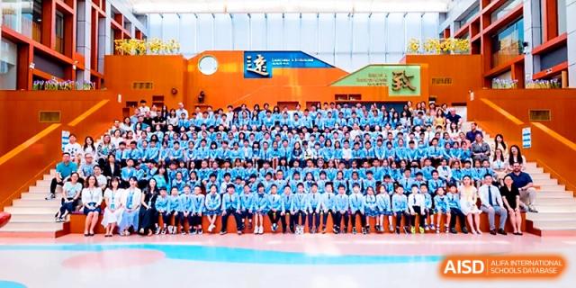 A large group of students in blue uniforms poses for a massive group photo in the gymnasium at Wahaha International School.