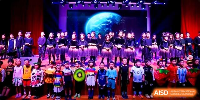 A group of students in vibrant costumes performs a choreographed routine on a brightly lit stage at Wahaha International School.