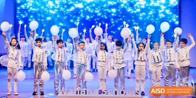 Students holding glowing balloons perform a magical finale during a school production at Wahaha International School.