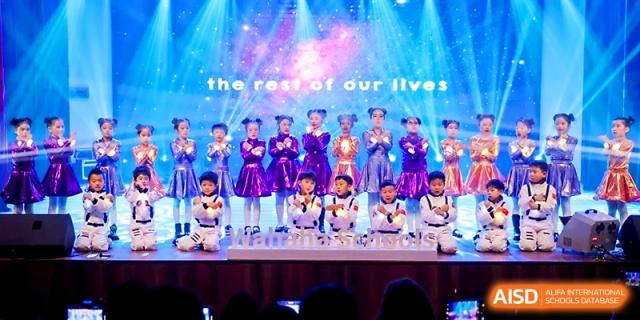 A choir of students in matching blue and silver outfits sings on stage for an audience at Wahaha International School.
